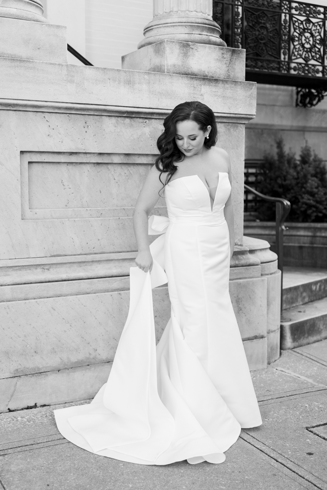 Black and white image of a bride in a satin gown with large bow