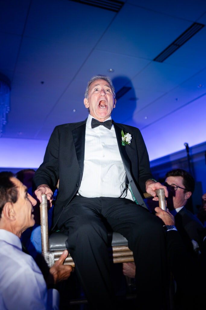Father of the bride laughing as he is lifted during the hora at Woodmont Country Club wedding reception
