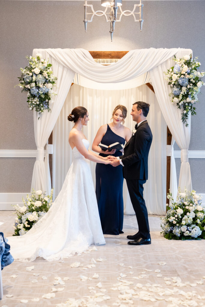 Indoor ceremony at Woodmont Country Club with bride and groom surrounded by family and friends.